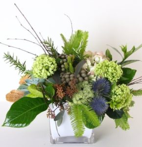 An assortment of textured, premium greenery and flowers, including thistle, hydrangea, succulents and more are included in this soothing design. Container may vary