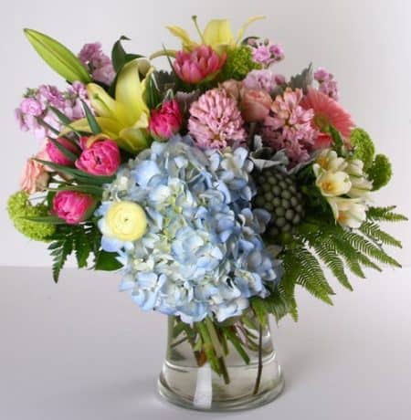 A lovely assortment of spring flowers in soft pastel colors is arranged in a glass vase. Included are hydrangea, tulips, hyacinth, stock and more. 