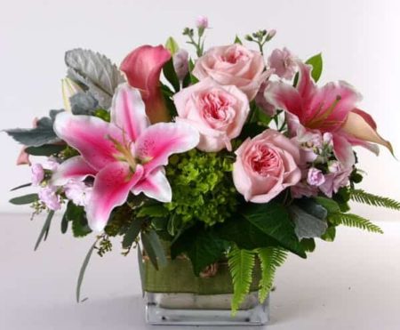 Pink roses, lilies, calla lilies, stock and assorted premium greens fill this glass cube vase.