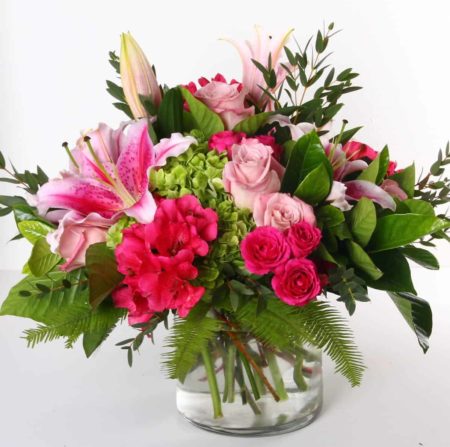 Bright pink and green flowers, including roses, hydrangea, and lilies are designed together in this cheerful cylinder arrangement. 