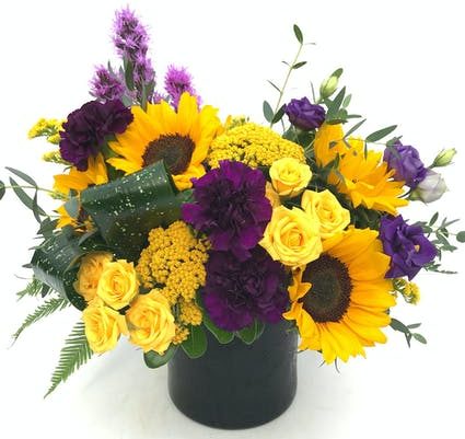 A beautiful combination of rich purple and bright yellow flowers, including sunflowers, spray roses, carnations, and more. 